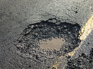 A pothole on the road, with a small amount of water pooled in.