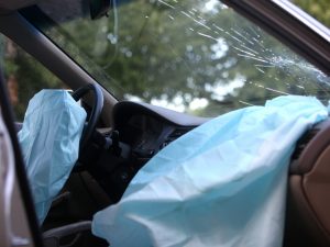 A car with a broken front window and blown out airbags